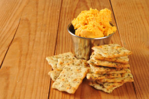 Italian herb flatbread crackers with bacon cheddar cheese spread on a rustic wooden surface